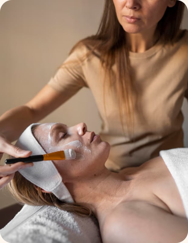 Esthetician applying a treatment mask with a brush to a client's face